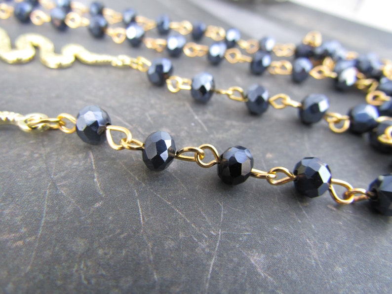 May include: A gold chain necklace with black faceted beads. The chain is made of small, delicate links.