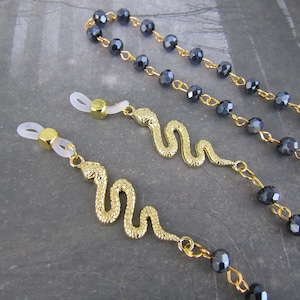May include: Two gold snake eyeglass chains with clear silicone end pieces. The chains are attached to black crystal beads.