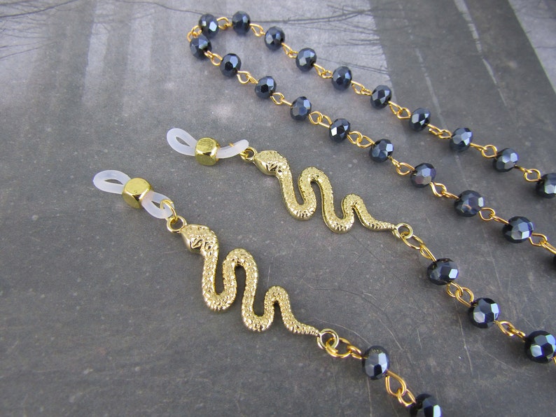 May include: Two gold snake eyeglass chains with clear silicone end pieces. The chains are attached to black crystal beads.