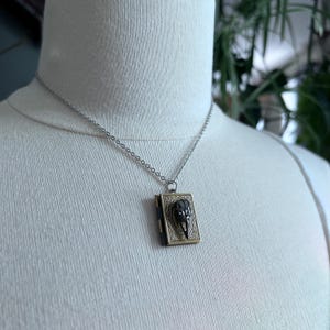 May include: A silver chain necklace with a gold locket pendant featuring a black skull design.