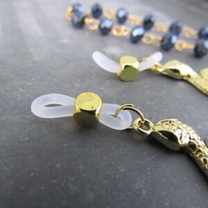 May include: Two gold-toned eyeglass chain ends. One end features a clear plastic loop with a gold-toned cube. The other end features a gold-toned snake charm.