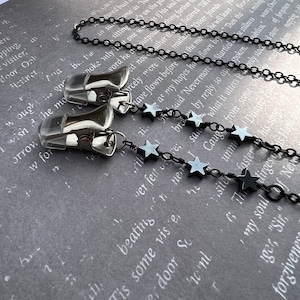 May include: A black chain necklace with silver clips and black star-shaped beads. The necklace is on a gray textured surface.