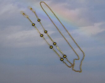 May include: A gold chain with small yellow and black flower accents. The chain has two clasps for attaching to glasses.