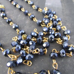 May include: A close-up of a dark blue crystal beaded necklace with gold chain links. The beads are faceted and have a shiny finish.
