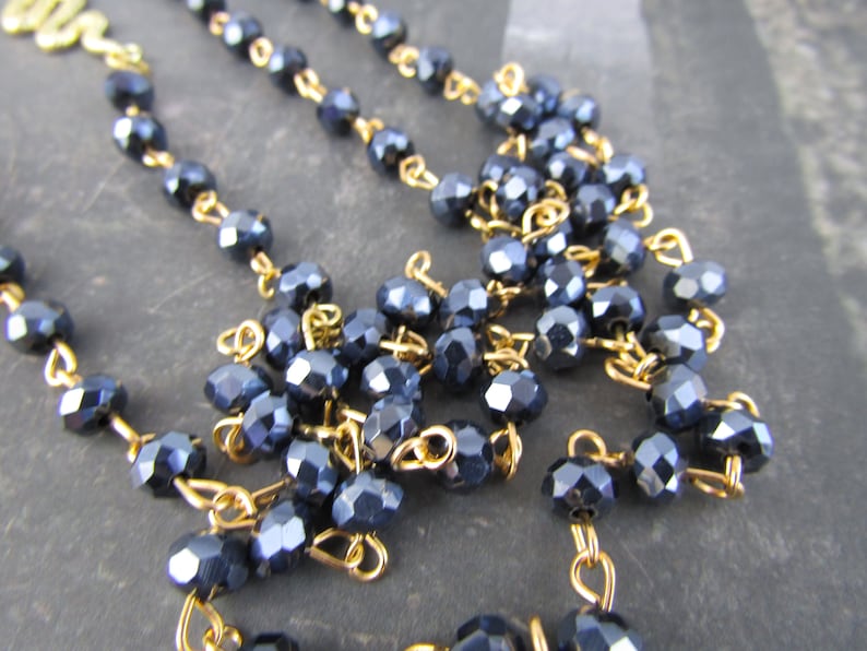 May include: A close-up of a dark blue crystal beaded necklace with gold chain links. The beads are faceted and have a shiny finish.
