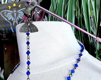 May include: A silver-toned moth-shaped eyeglass holder with a chain of blue beads. The eyeglass holder is attached to a pair of pink eyeglasses. The necklace is made of blue beads.