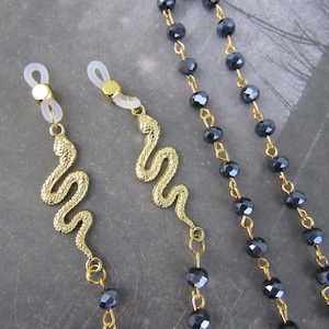 May include: Two gold snake eyeglass chains with black crystal beads. The chains have clear plastic clasps for attaching to glasses.