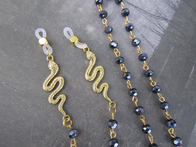 May include: Two gold snake eyeglass chains with black crystal beads. The chains have clear plastic clasps for attaching to glasses.