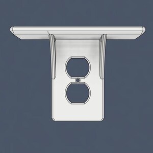 May include: A white wall-mounted shelf with an integrated dual-outlet electrical faceplate. The shelf features a flat horizontal surface supported by two vertical brackets that frame the standard duplex receptacle opening in the center.