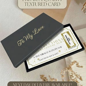 May include: A black rectangular gift box with the gold text To My Love on the lid. Inside, a white card features the text CONGRATULATIONS ON YOUR BEAUTIFUL NEWS, A TINY MIRACLE IS ON ITS WAY, and LOVE FROM ALLY & MATT, with a gold scratch-off panel.