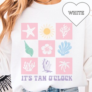 May include: White sweatshirt with a pink and blue graphic design of various sea life and the text "IT'S TAN O'CLOCK".