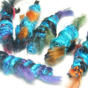May include: Six colorful yarn wrapped ornaments in shades of blue, black, orange, green, and purple. The ornaments are made of yarn and are twisted into a spiral shape.