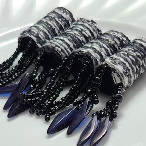 May include: Four black and white patterned hair rollers with black beads and blue iridescent fringe.