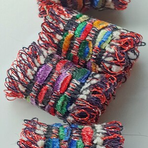 May include: Four colorful woven fingertip thimbles with red, white, blue, green, purple, and orange stripes. The thimbles have a fringe of red and black thread.