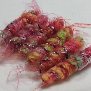 May include: A close-up of a group of colorful yarn wrapped around a wire, creating a unique and textured design. The yarn is pink, green, yellow, and orange, with a silver wire running through it. The yarn is fluffy and soft, and the wire gives it a bit of structure.