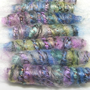 May include: A collection of colorful, hand-crafted beads made from yarn and fabric. The beads are twisted and have a fuzzy texture. They are in shades of blue, green, purple, and white.