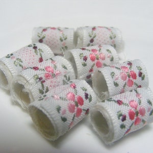 May include: A group of white fabric spools with pink and green floral patterns. The spools are arranged in a circle.