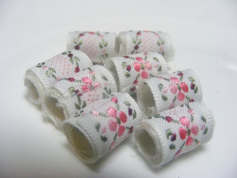 May include: A group of white fabric spools with pink and green floral patterns. The spools are arranged in a circle.
