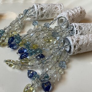 May include: Three white lace-covered spools with blue, yellow, and clear crystal beads hanging from them.