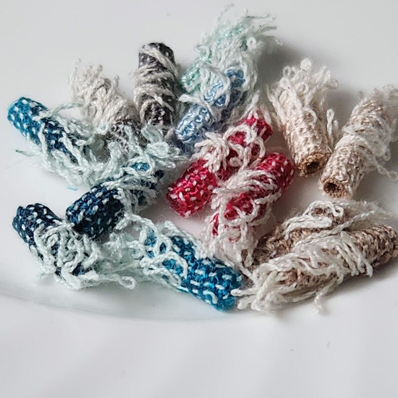 Może przedstawiać: Zestaw kolorowych nici owiniętych wok&oacute;ł małych drewnianych kołk&oacute;w, z postrzępionymi końcami. Nici są w odcieniach niebieskiego, białego, czerwonego i brązowego.