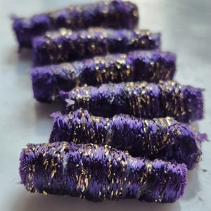 May include: A close-up of a pile of purple and gold trim. The trim is made of a soft, textured fabric with a subtle sheen. The trim is perfect for adding a touch of elegance to any project.