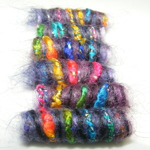 May include: A collection of colorful yarn wrapped around a base, creating a series of colorful, fuzzy, and textured cylinders. The yarn is a mix of purple, blue, green, orange, yellow, and pink.