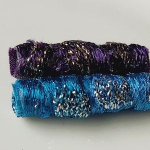May include: Two spools of thread, one purple with gold accents and one blue with silver accents.