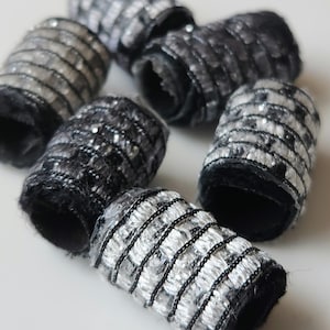 May include: Close-up of six black and silver fabric rolls with a textured, woven design. The rolls are arranged in a semi-circle on a white surface.