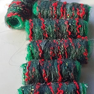 May include: Close-up of six spools of green and red yarn. The yarn is a mix of green, red, and black fibers. The spools are stacked on top of each other.
