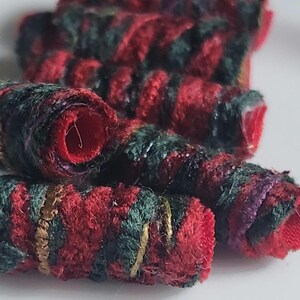 May include: A collection of cylindrical beads featuring a textured, wrapped design. The beads are composed of alternating diagonal stripes in deep red, dark green, and metallic gold thread, with a hollow center visible in each bead.