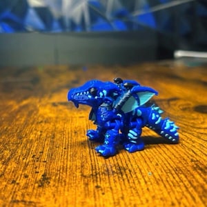 Pu&ograve; includere: Una piccola statuetta di drago articolata in una vibrante tonalit&agrave; di blu reale. La creatura presenta accenti color ciano pi&ugrave; chiari lungo le ali, la schiena e le zampe, con una superficie squamata e testurizzata e una testa dai tratti definiti.