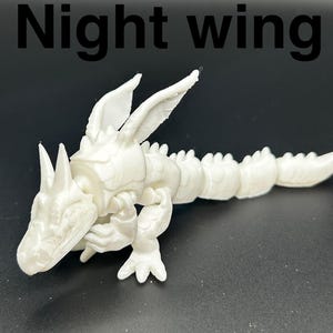 Op de afbeelding: Een wit, beweeglijk draakspeelgoed met de tekst "Night wing" in het zwart. De draak heeft een gedetailleerd ontwerp met vleugels, hoorns en een gesegmenteerd lichaam. Het speelgoed is gemaakt van 3D-geprint materiaal.