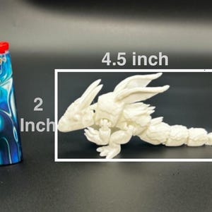 Op de afbeelding: Een witte, beweegbare drakenfiguur, ongeveer 11,4 cm lang, naast een 5,1 cm hoge blauw-witte BIC aansteker. De draak heeft gedetailleerde vleugels en een gesegmenteerd lichaam, wat wijst op een fantasiethema.