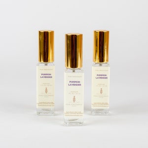May include: Three perfume bottles with gold lids and clear glass bodies. Each bottle has a label that reads "Pumpkin Lavender" and "Perfume 1 fl oz / 30 ml". The bottles are from Pink Parchment.