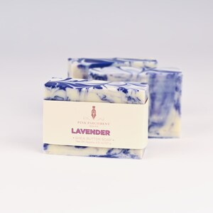 May include: Lavender shea butter soap bars with a white and blue marbled design. The soap is wrapped with a cream-colored label that reads "Pink Parchment Soaps Lavender". Each bar weighs approximately 4.5 oz.