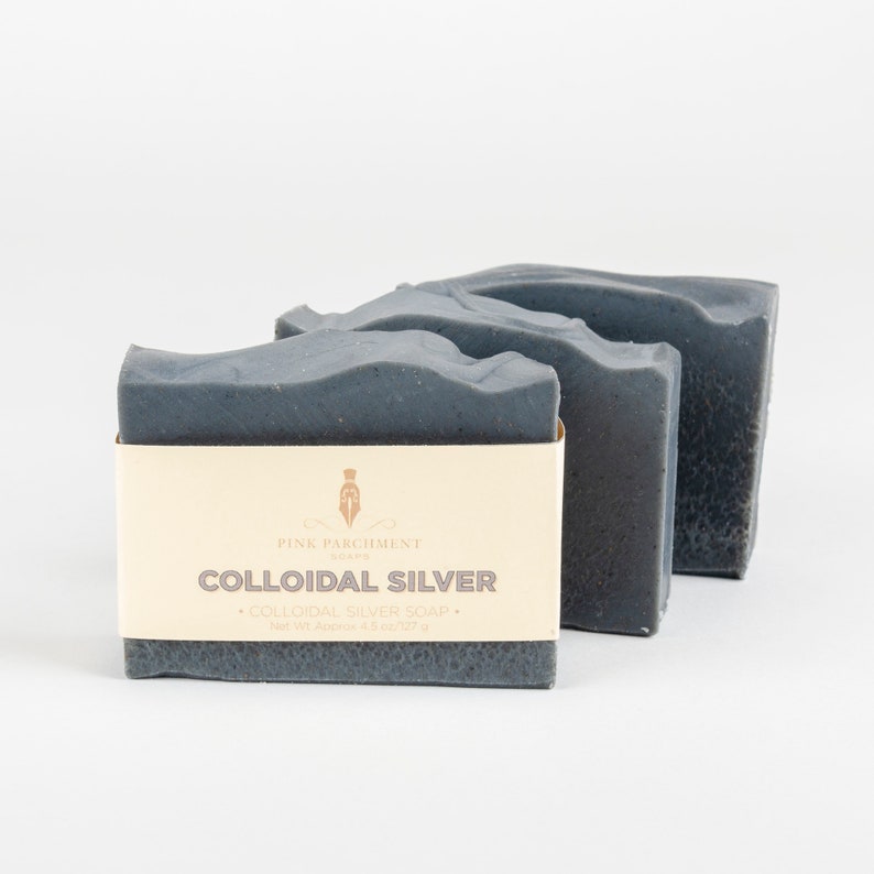 May include: Three dark gray bars of soap are arranged on a white background. The front bar has a cream-colored label with the text "COLLOIDAL SILVER" and "COLLOIDAL SILVER SOAP". The net weight is approximately 4.5 oz / 127 g.