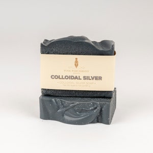 May include: Two bars of colloidal silver soap. The soap is dark gray with white speckles and a textured surface. A beige label wraps around the top bar, displaying the text "Pink Parchment Soaps" and "Colloidal Silver". Net weight is approximately 4.5 oz.