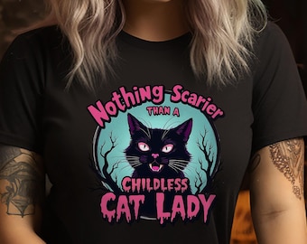 May include: Black t-shirt with a graphic of a black cat with pink eyes and a pink mouth. The text "Nothing Scarier Than A Childless Cat Lady" is written in pink on a blue circle.