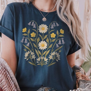 May include: Navy blue t-shirt with a floral design featuring daisies, yellow flowers, and bellflowers. The graphic is centered on the front. The shirt has short sleeves and a crew neck.