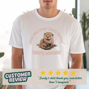 May include: White t-shirt with a brown otter illustration and the text "Just me over here being Otterly adorable".