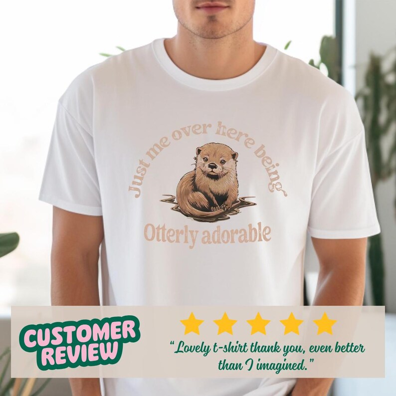 May include: White t-shirt with a brown otter illustration and the text "Just me over here being Otterly adorable".