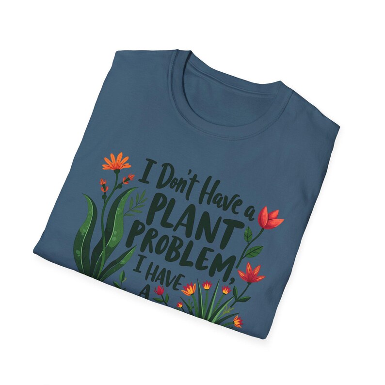 May include: A navy blue t-shirt, folded, featuring the text "I Don't Have a PLANT PROBLEM, I HAVE A..." and floral illustrations in orange and green. The shirt has a crew neck.