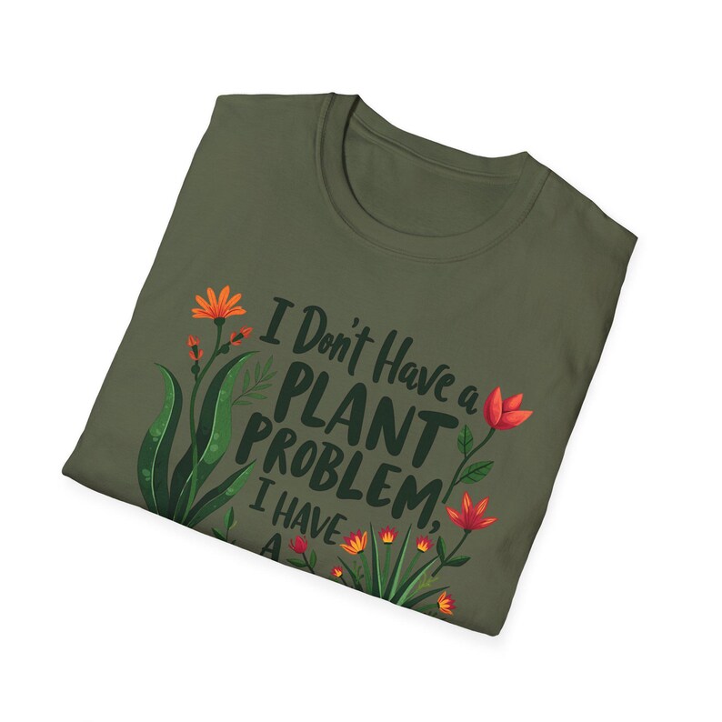 May include: Khaki green t-shirt featuring the text "I Don't Have a PLANT PROBLEM, I HAVE A..." and floral designs in orange and red. The shirt is folded and presented against a white backdrop.