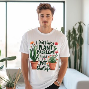 May include: White t-shirt with the text "I Don't Have a Plant Problem, I Have a Pot Shortage." The shirt features illustrations of plants in terracotta pots with colorful flowers. The design is centered on the front of the shirt.