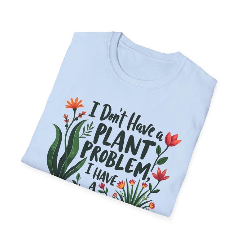 May include: Pale blue t-shirt with the slogan "I Don't Have a Plant Problem, I Have a Plant Collection". The design includes green leaves and orange and red flowers, giving a botanical theme.