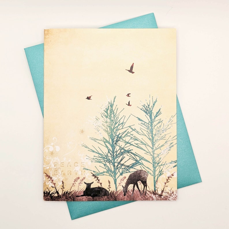 May include: A greeting card with a nature scene featuring deer, trees, and birds in flight. The card has a cream-coloured background with teal trees and a teal envelope. The words "PEACE EARTH" are printed on the card.