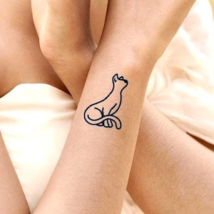 Peut inclure: Tatouage minimaliste d'un chat noir sur un bras. Le chat est représenté assis, regardant vers le haut. Le tatouage est un design simple et élégant, idéal pour les amoureux des chats.