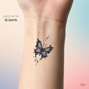 Peut inclure: Un tatouage temporaire d'un papillon bleu foncé sur un poignet. Le papillon présente des détails complexes sur les ailes et est entouré de fines lignes. Le texte indique "LASTS UP TO 15 DAYS".