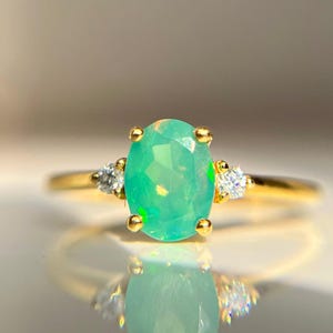 May include: A gold ring with a green opal gemstone and two smaller diamond accents.
