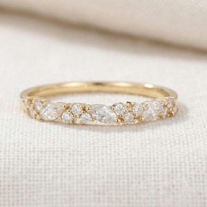 Puede incluir: Un anillo de banda dorada con una serie de piedras transparentes alternadas en talla marquesa y redonda a lo largo de la mitad superior. El metal tiene un acabado en oro amarillo pulido y las piedras están dispuestas en un patrón.